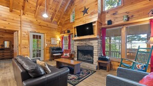 A log cabin interior with a fireplace, wooden furniture, and large windows. - Nestled in a scenic backdrop with captivating mountain valley view (Rogers)