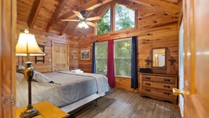 A wooden cabin bedroom with a bed, dresser, and a ceiling fan. - Nestled in a scenic backdrop with captivating mountain valley view (Rogers)