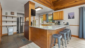 A modern kitchen with wooden cabinets, a stainless steel refrigerator, a granite countertop, and bar stools. - Updated Lake House, set atop the hill overlooking beautiful Deer Water Lake. (Rogers)