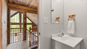 A wooden interior with a bathroom featuring a white sink, mirror, and towel rings. - Updated Lake House, set atop the hill overlooking beautiful Deer Water Lake. (Rogers)