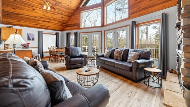 A spacious living room with a wooden ceiling, large windows, a fireplace, and leather furniture. - Updated Lake House, set atop the hill overlooking beautiful Deer Water Lake. (Rogers)