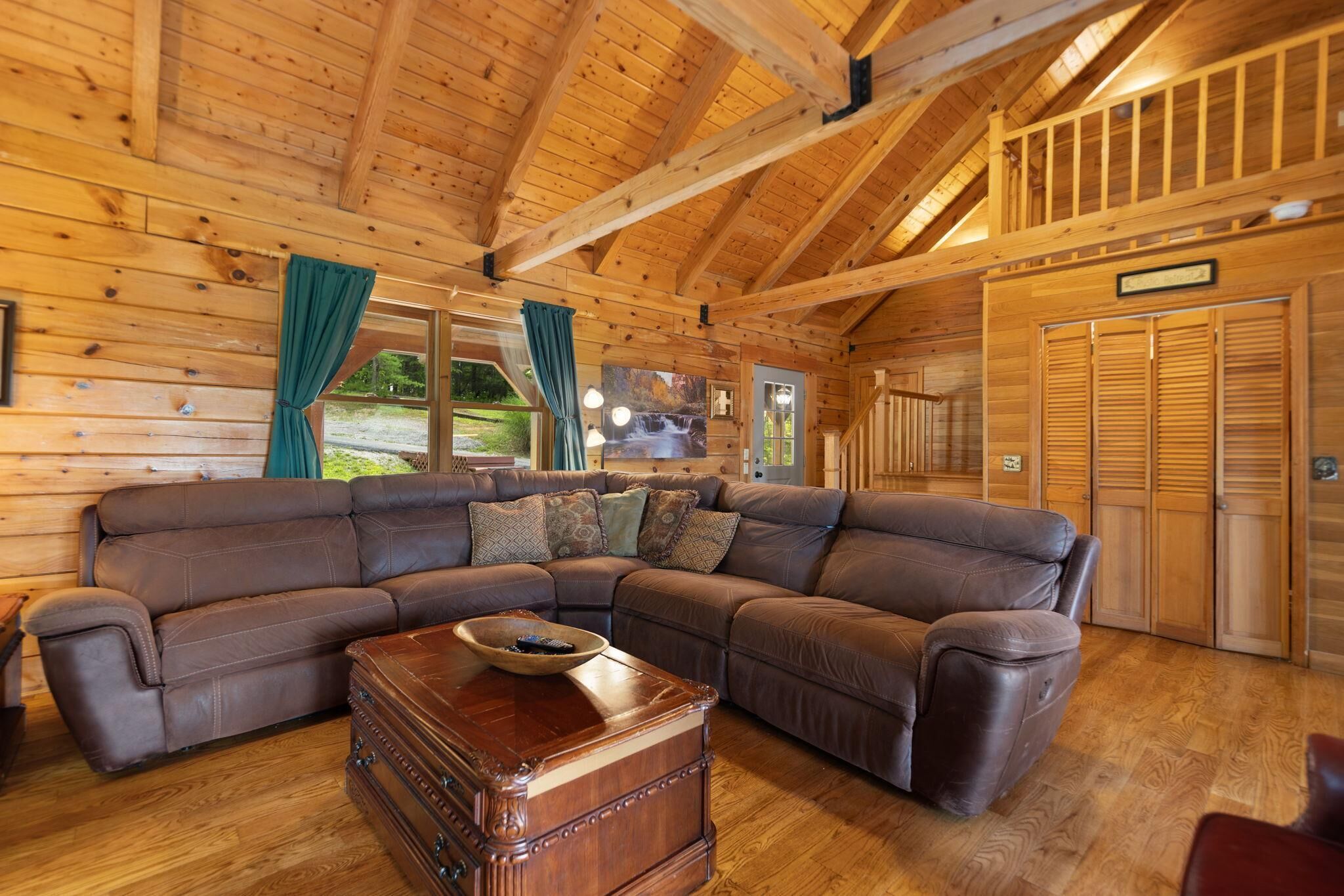 L’intérieur d’un chalet en bois est aménagé avec un grand canapé d’angle, une commode en bois et un espace de couchage en mezzanine.