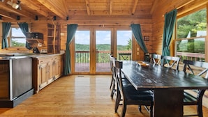 A wooden cabin with a kitchen, dining area, and large windows offering a view of the outdoors. - Large Luxury Log Cabin, Sleeps-13, Spectacular view! Loaded with ammenities! (Rogers)