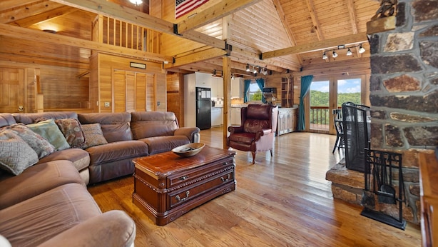 A spacious living area with a wooden ceiling, a leather sofa, a coffee table, and a stone fireplace. - Large Luxury Log Cabin, Sleeps-13, Spectacular view! Loaded with ammenities! (Rogers)