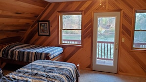 Een slaapkamer in een blokhut met twee bedden, houten wanden en een deur naar een terras.