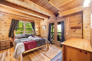 A wooden cabin bedroom with a bed, bedside table, and a view through a window.