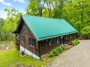 A wooden cabin with a green roof, a porch, and a gravel driveway. - Large Log home, private pond with dock, pool table, hot tub & internet. (Rogers)