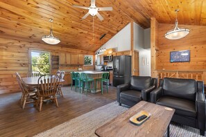 A spacious cabin with a wooden interior, a dining area with green chairs, a kitchen with modern appliances, and a leather sofa. - Spacious cabin with 2 living rooms! (Rogers)