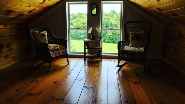 Ein gemütliches Schlafzimmer im Dachgeschoss mit Holzwänden und geneigter Decke. Zwei Schaukelstühle und ein kleiner Tisch mit Lampe sind vorhanden.