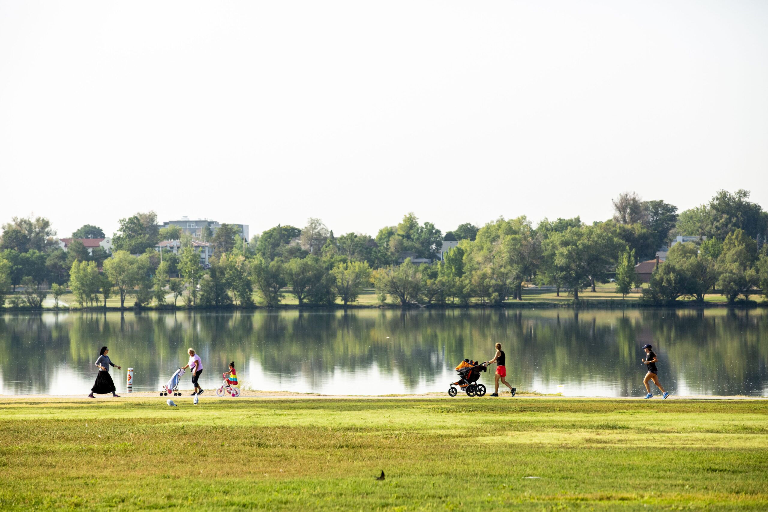 A park with a lake, trees, and people walking.