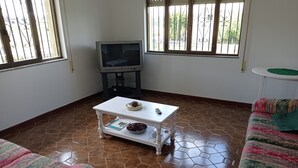 Un salon avec un téléviseur, une table basse blanche, des canapés à motifs et un sol carrelé.