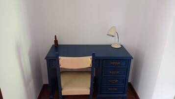 Un escritorio azul oscuro pequeño con una silla color beige, una lámpara de escritorio blanca y un adorno pequeño sobre el escritorio.