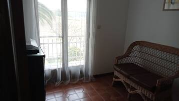 Una habitación con un sofá de mimbre, un piano y un ventanal con cortinas de gasa.