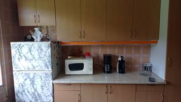 A kitchen with wooden cabinets, a marble-patterned refrigerator, a microwave, a coffee maker, and a kettle.