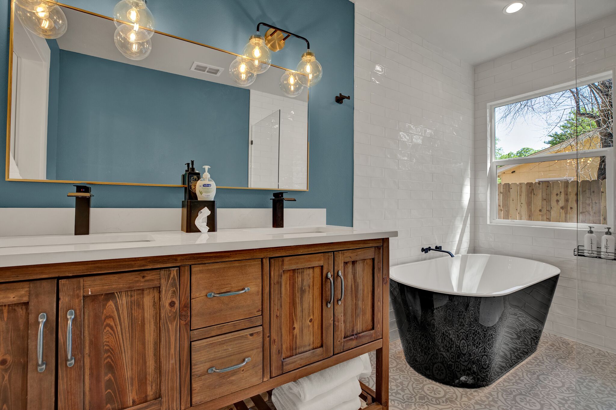 A bathroom with a wooden vanity, a large mirror, and a freestanding bathtub.