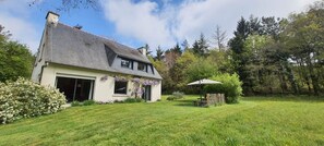 Une maison avec un toit en pente, un garage et une pelouse agrémentée d’une table de patio et d’un parasol.