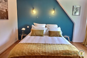 A bedroom with a bed, two bedside tables, a nightstand, and a wall-mounted light fixture.