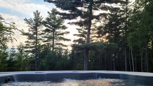 A hot tub surrounded by tall trees and a clear sky. - Spacious house with pebble beach. Direct access to Snowmobile and ATV trails! (Beaver Cove)