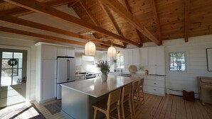 A spacious kitchen with wooden beams, white cabinetry, and a central island with bar stools. - Spacious house with pebble beach. Direct access to Snowmobile and ATV trails! (Beaver Cove)