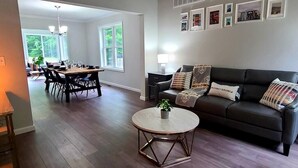 Un salon moderne avec un canapé en cuir foncé, une table basse ronde et un coin repas comprenant une table et des chaises en bois.