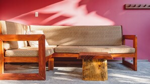 A wooden sofa with patterned cushions against a red wall, a matching wooden coffee table, and a wall-mounted coat rack. - Iluminar Beachfront Suite (Nosara)