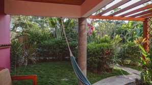 A hammock hanging between wooden pillars in a garden with a grassy area and various plants. - Iluminar Beachfront Suite (Nosara)