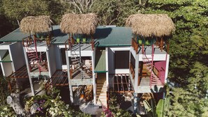 A multi-story building with thatched-roof structures, staircases, and a garden area. - Iluminar Beachfront Suite (Nosara)