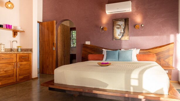 A bedroom with a wooden bed, a nightstand, a wall-mounted air conditioner, and a wooden wardrobe. - Iluminar Beachfront Suite (Nosara)