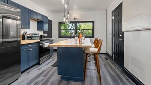 Una cocina moderna con armarios azul oscuro, una isla central con taburetes, electrodomésticos de acero inoxidable y un amplio ventanal que proporciona luz natural.