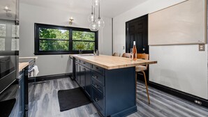 Una cocina moderna con una isla grande, armarios negros, encimera de madera y una ventana con vistas a zonas verdes.