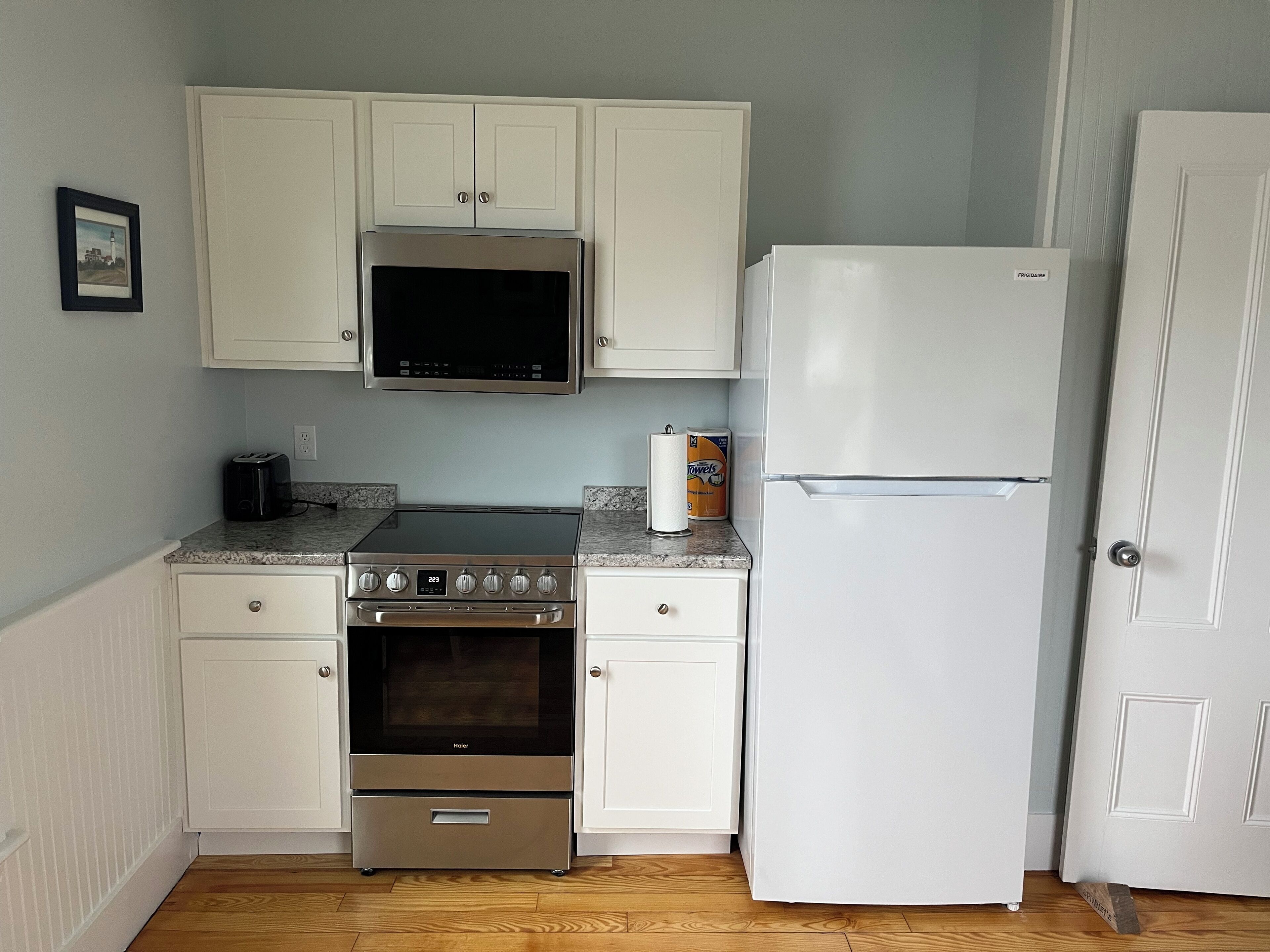 A compact kitchen with white cabinets, a stainless steel stove, a microwave, and a white refrigerator.