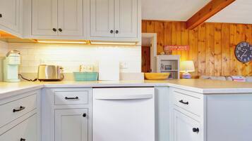 A kitchen with white cabinets, a dishwasher, a toaster, and a coffee maker. There is a wooden wall and a clock on the wall.
