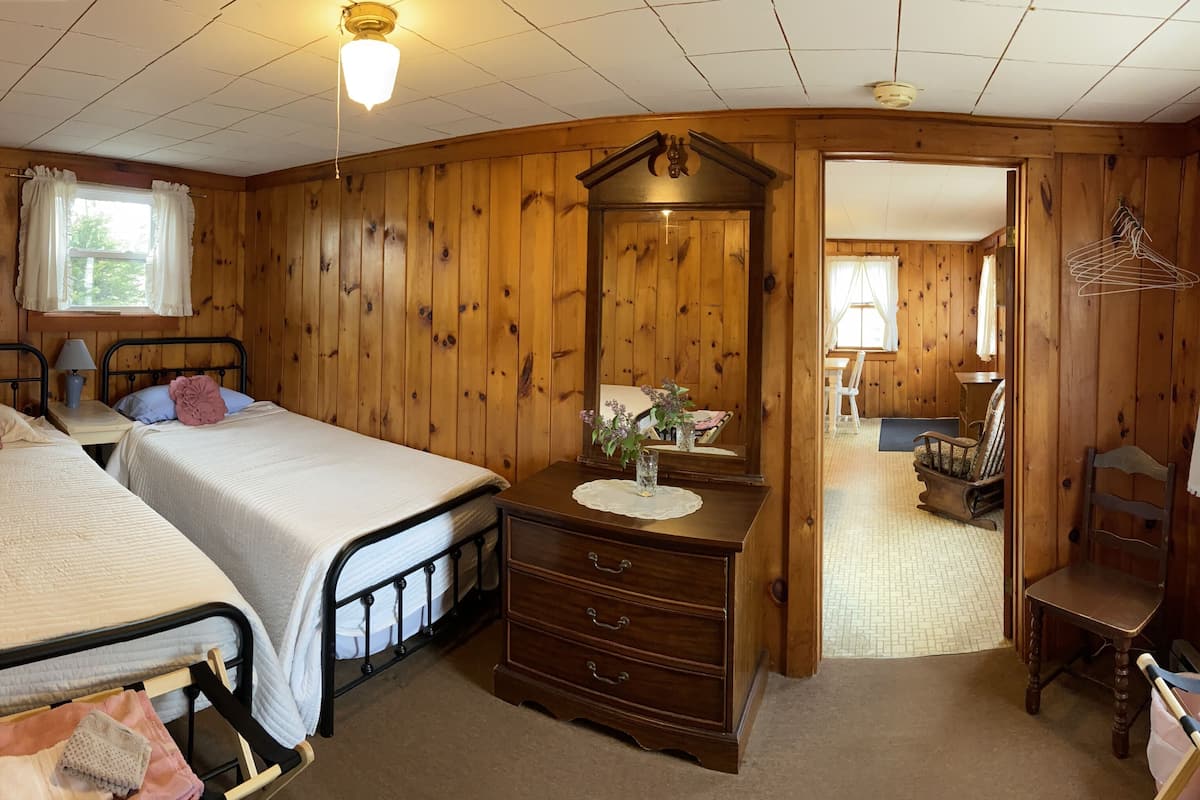 A cozy room with two beds, a wooden dresser, a mirror, and a chair.