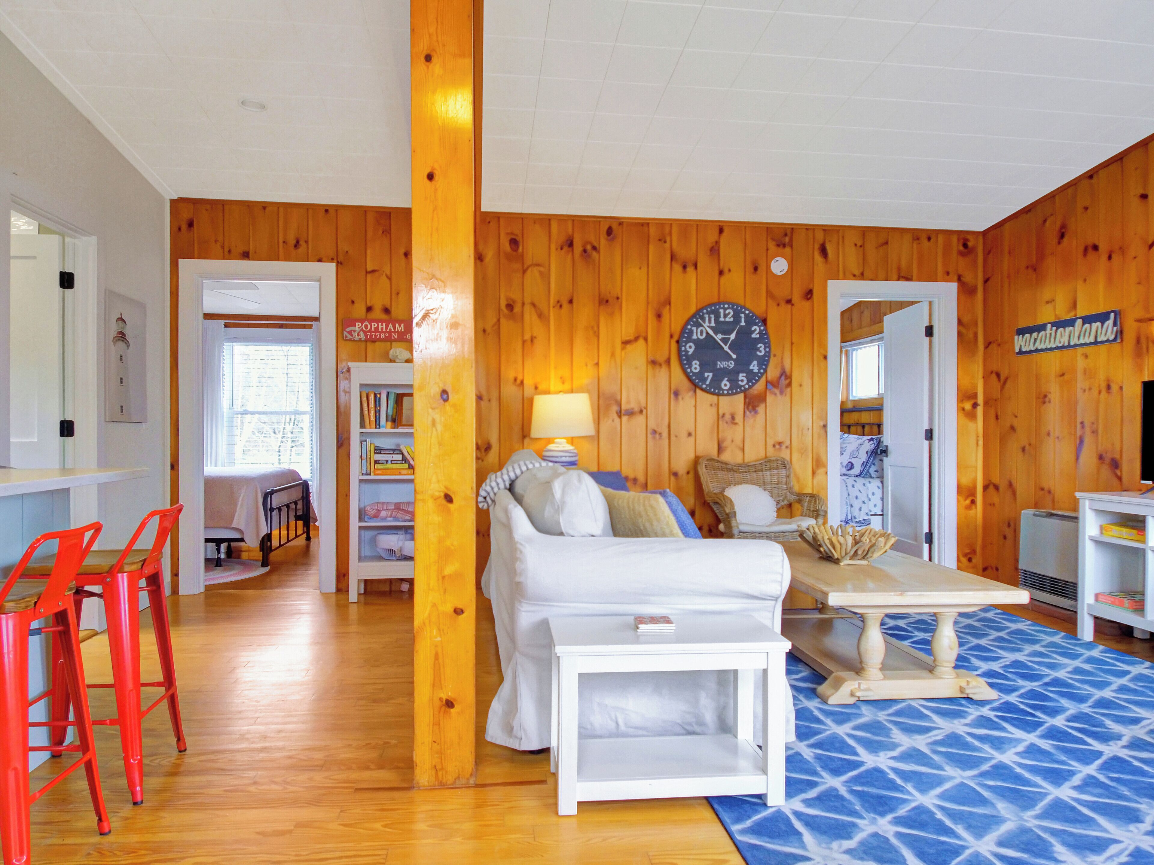 Una habitación acogedora con una pared de madera, un sofá blanco, una mesita pequeña y una silla roja.