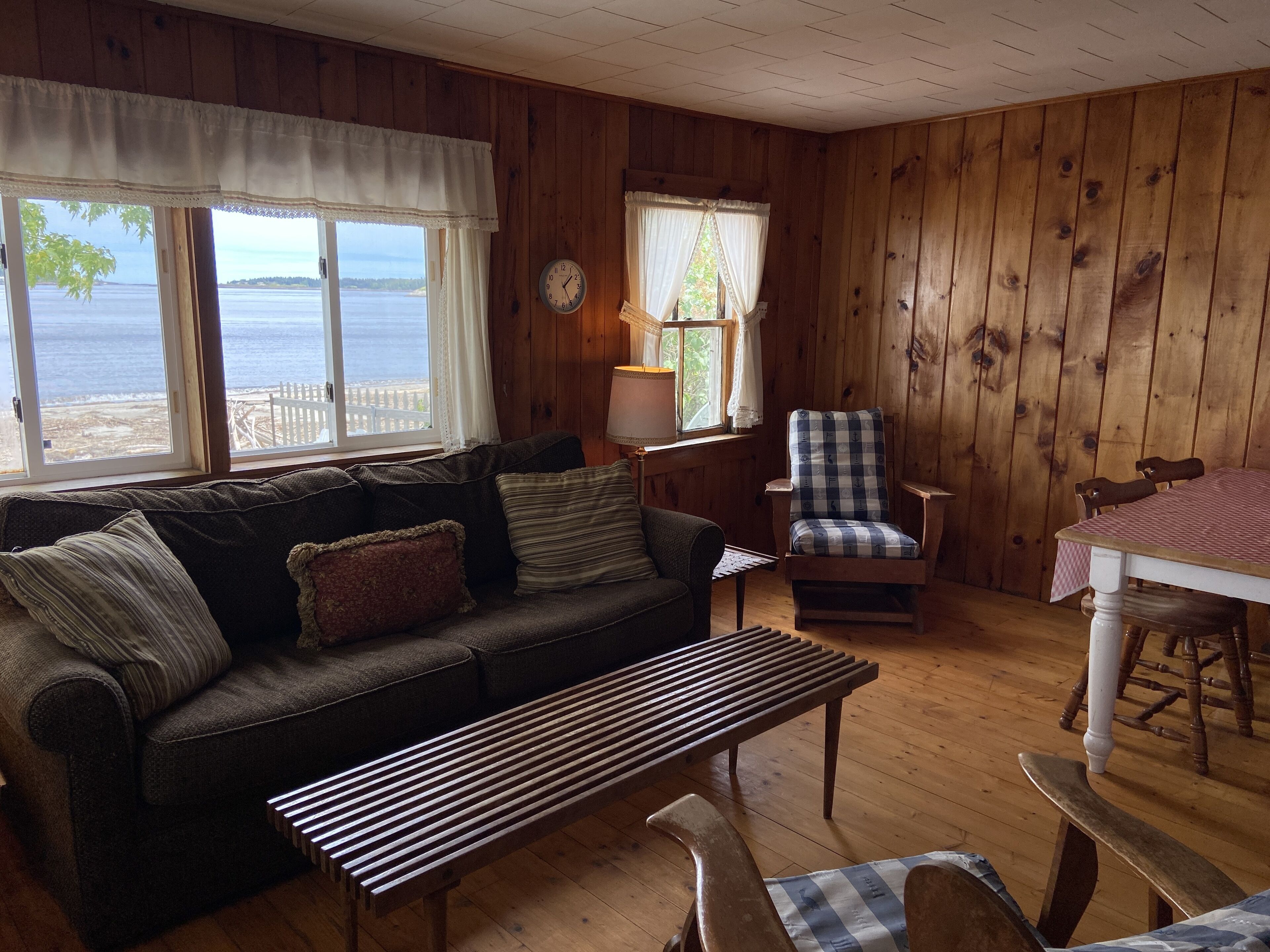 A cozy cabin interior with a wooden floor, a sofa, a bench, a dining table, and a chair.
