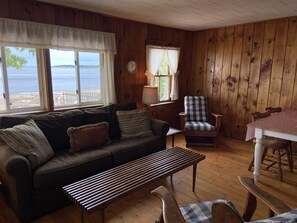 Interior acogedor de una cabaña con piso de madera, un sofá, un banco, una mesa de comedor y una silla.