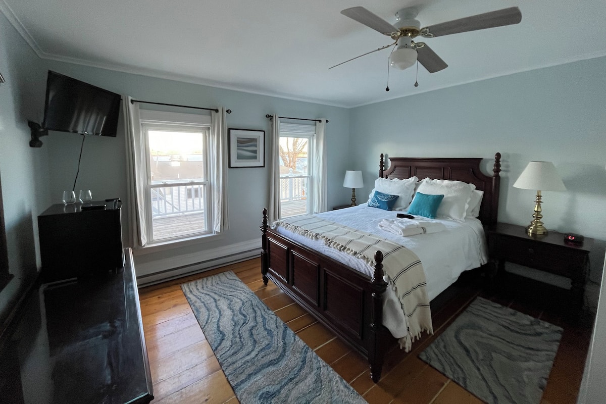 A bedroom with a bed, a ceiling fan, a TV, and a window.