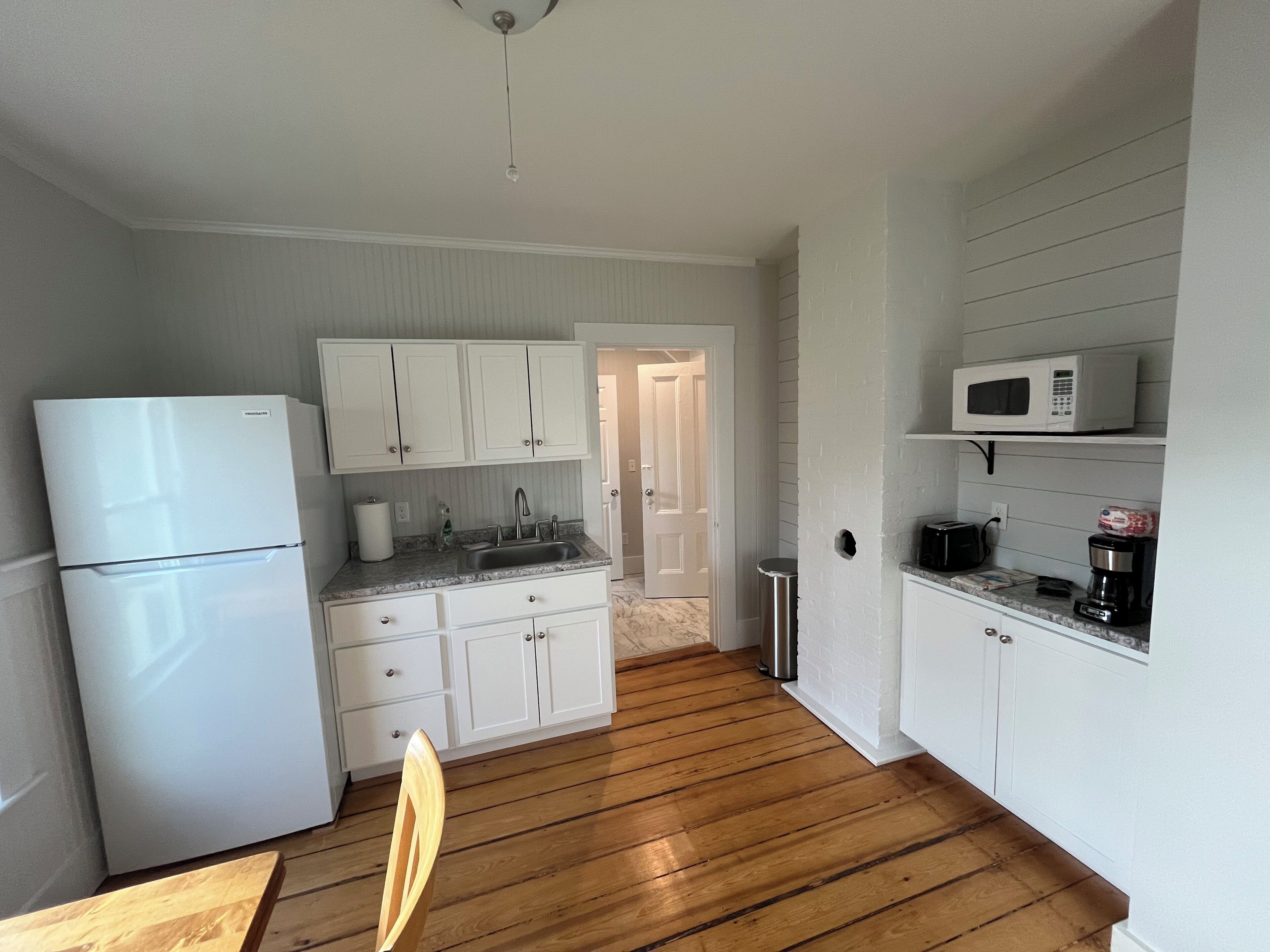 A compact kitchen with white cabinets, a stainless steel sink, a microwave, and a coffee maker.