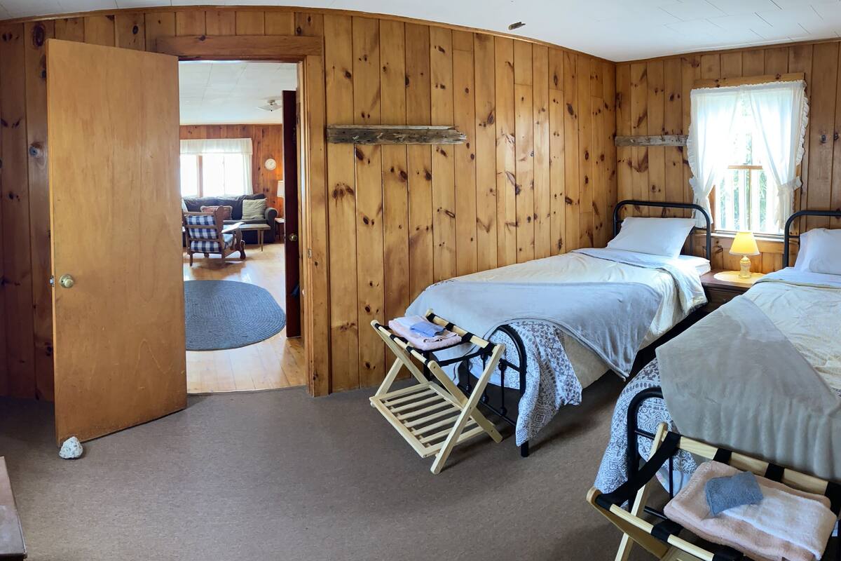 A wooden cabin bedroom with two beds, a wooden dresser, and a small table.