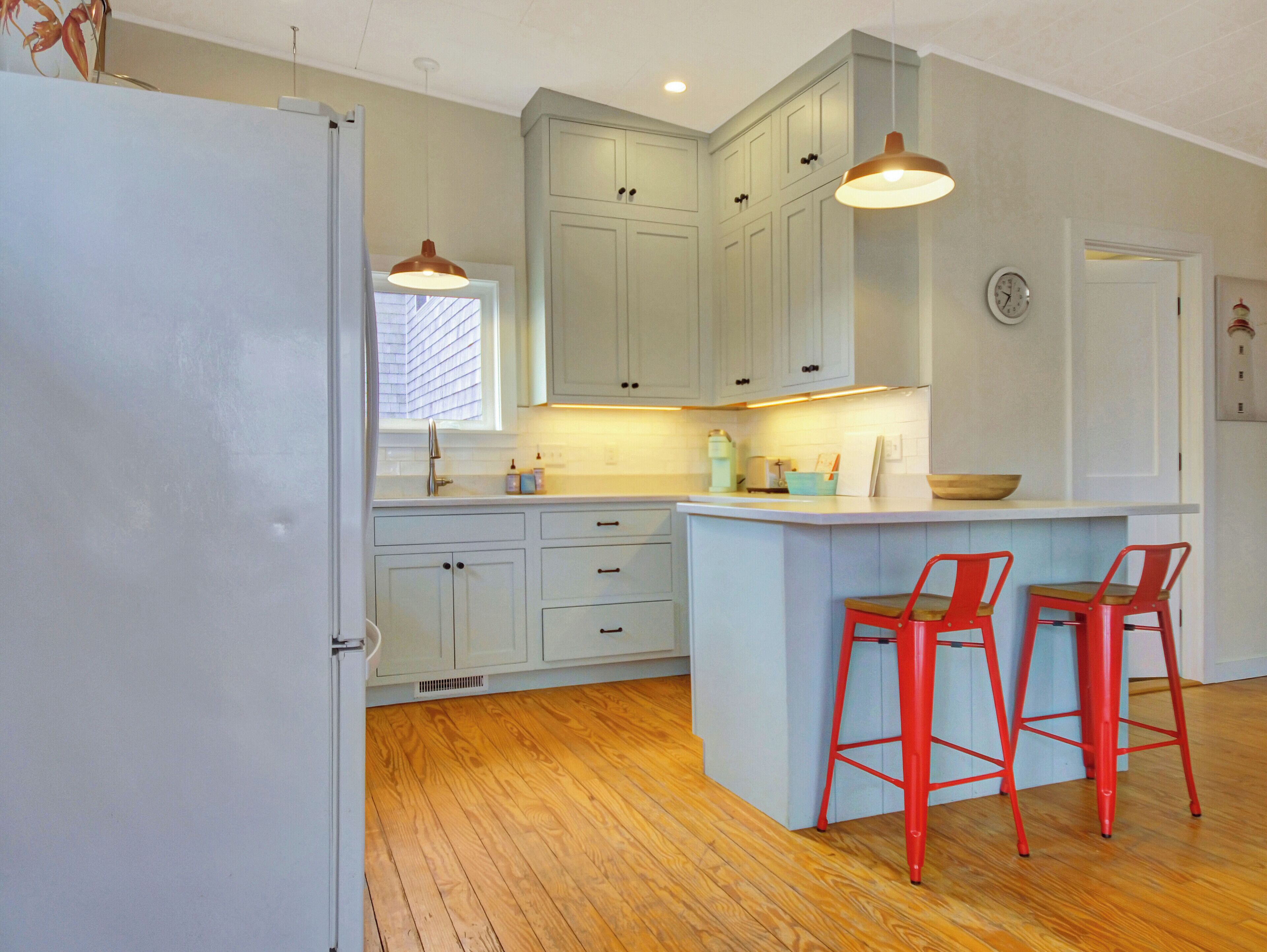 A kitchen with light blue cabinets, a wooden floor, and two red bar stools.