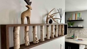 Uma prateleira de madeira com objetos decorativos, incluindo uma figura de veado, uma escultura de pássaro e um pinhão.
