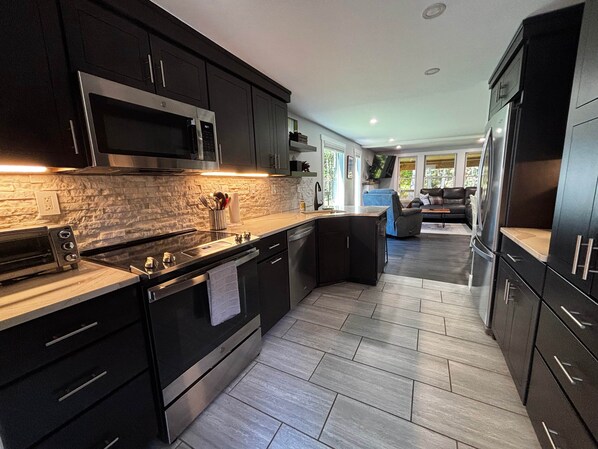 A modern kitchen with dark cabinetry, stainless steel appliances, and a herringbone-patterned floor.
