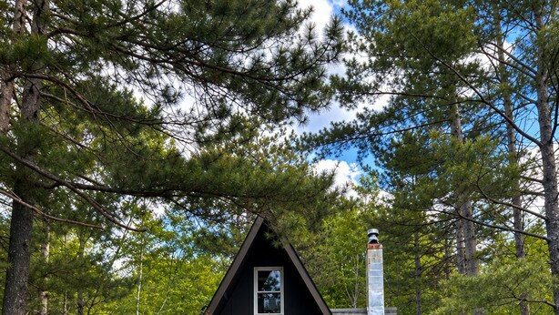 Une cabane avec une terrasse, un foyer et des fauteuils Adirondack rouges.