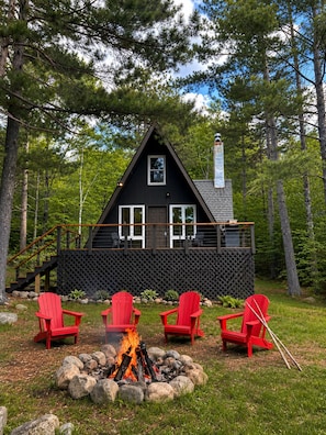 Eine Hütte mit einer Terrasse, einer Feuerstelle und roten Adirondack-Stühlen.