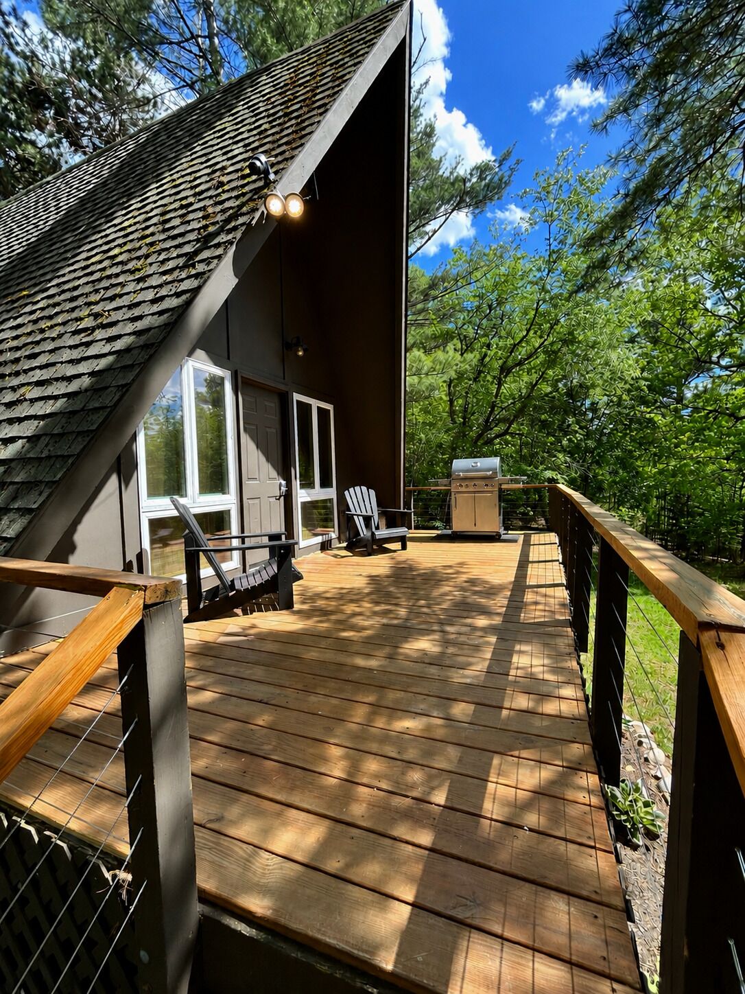 A wooden deck with a view of a house, a grill, and two chairs.