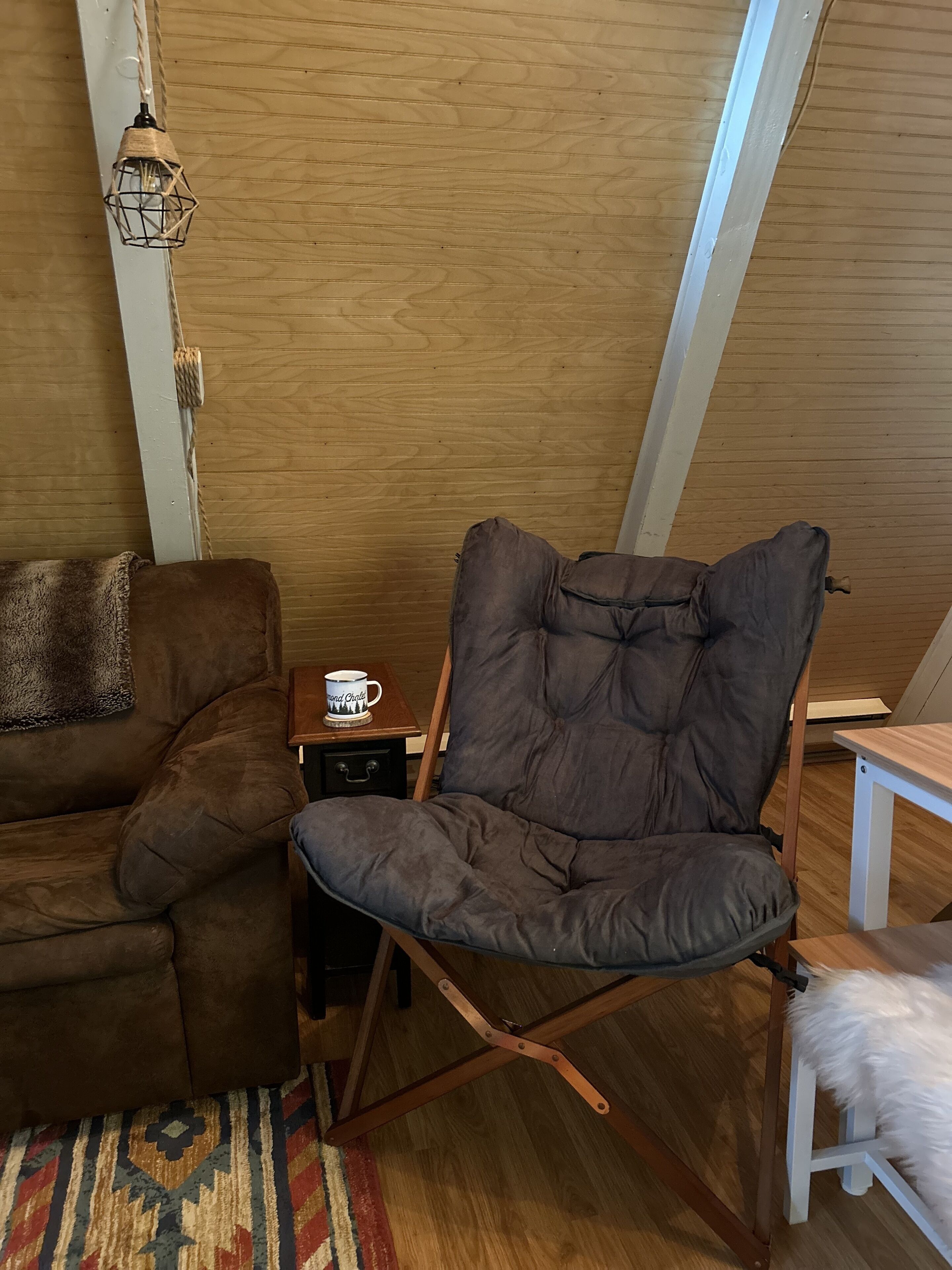 Ett mysigt rum med en brun lädersoffa, en bekväm fåtölj, ett litet träbord med en mugg på och en mönstrad matta.