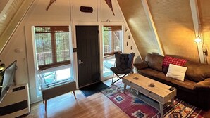 Un salon chaleureux de style industriel, avec un plafond en bois, un canapé, une table basse et une grande fenêtre.