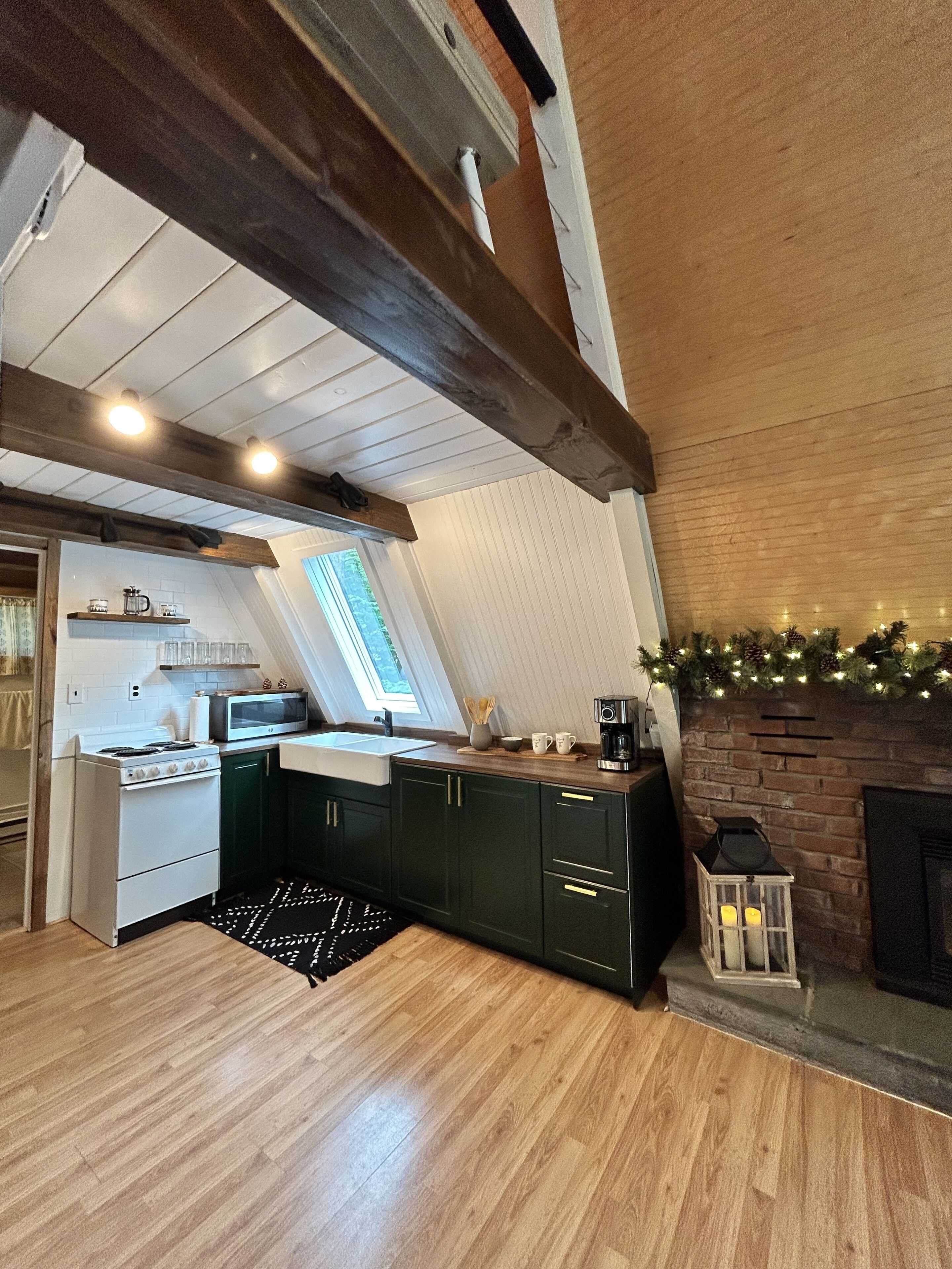 A kitchen with a built-in stove, microwave, and sink, wooden flooring, and a brick fireplace.
