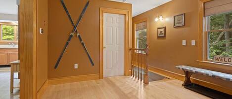 A hallway with wooden floors, a white door, and a bench with a 'WELCOME' sign.