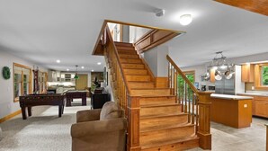 Un vaste espace de vie agrémenté d’un escalier en bois, d’une table de billard et d’un coin salon confortable.